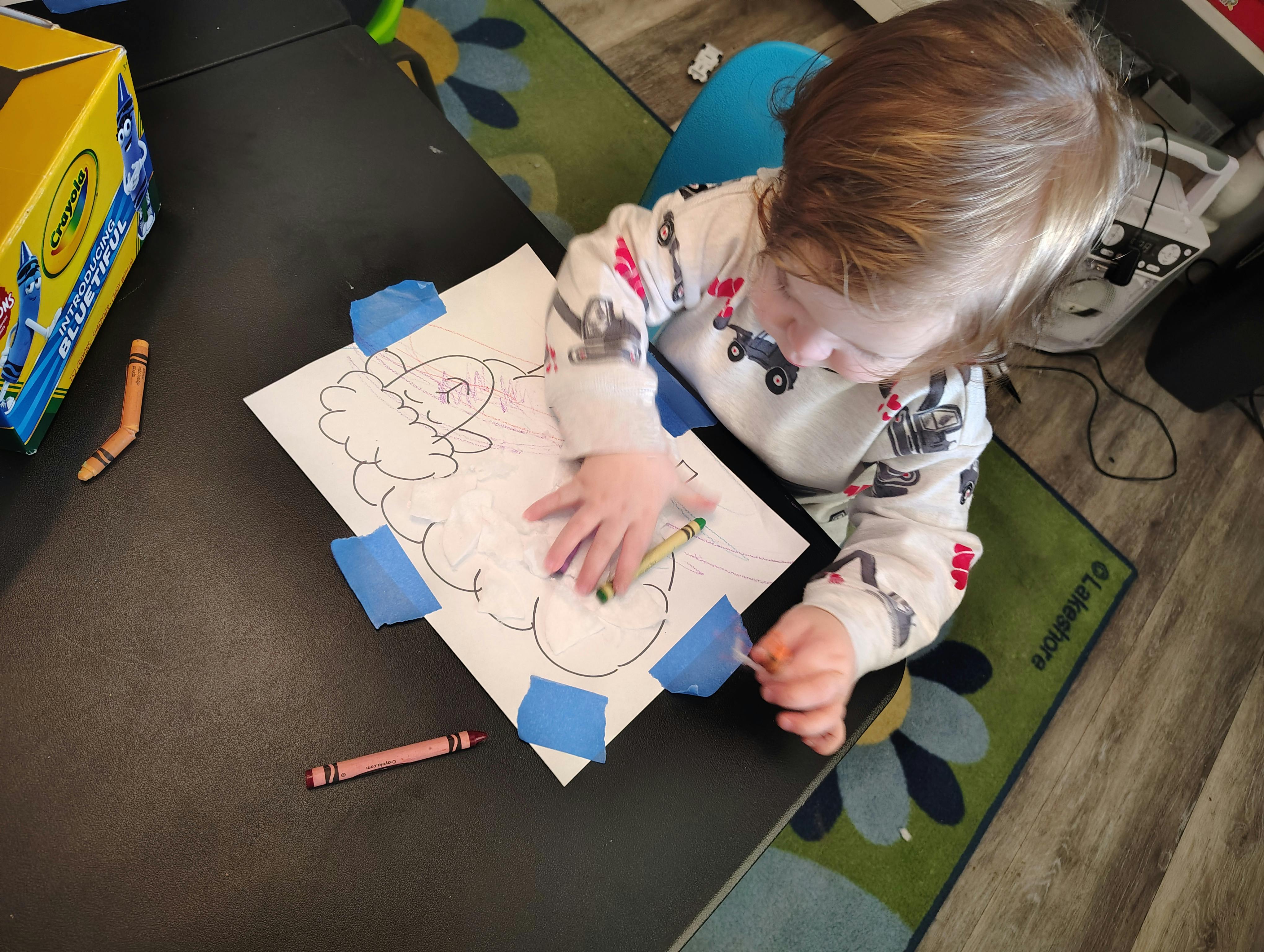 child coloring a picture of a sheep with crayons at a table