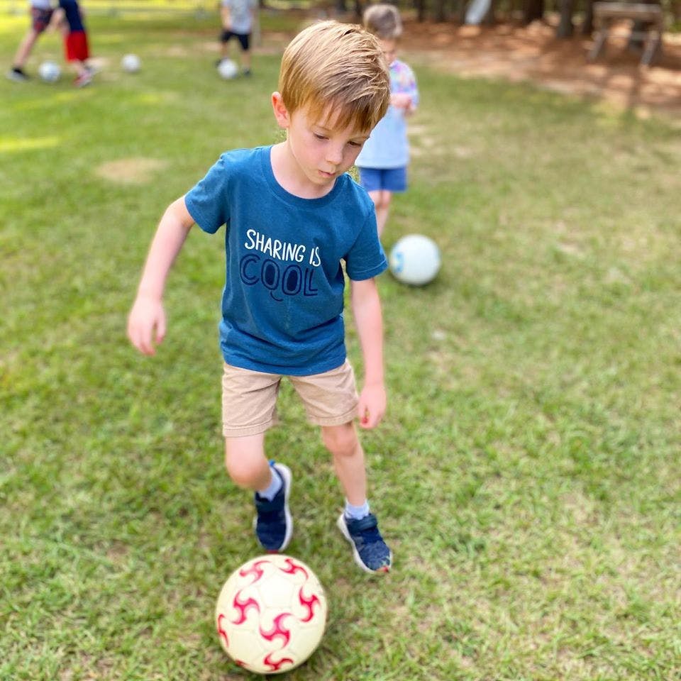 Child in a blue shirt kicking a soccer ball on grass