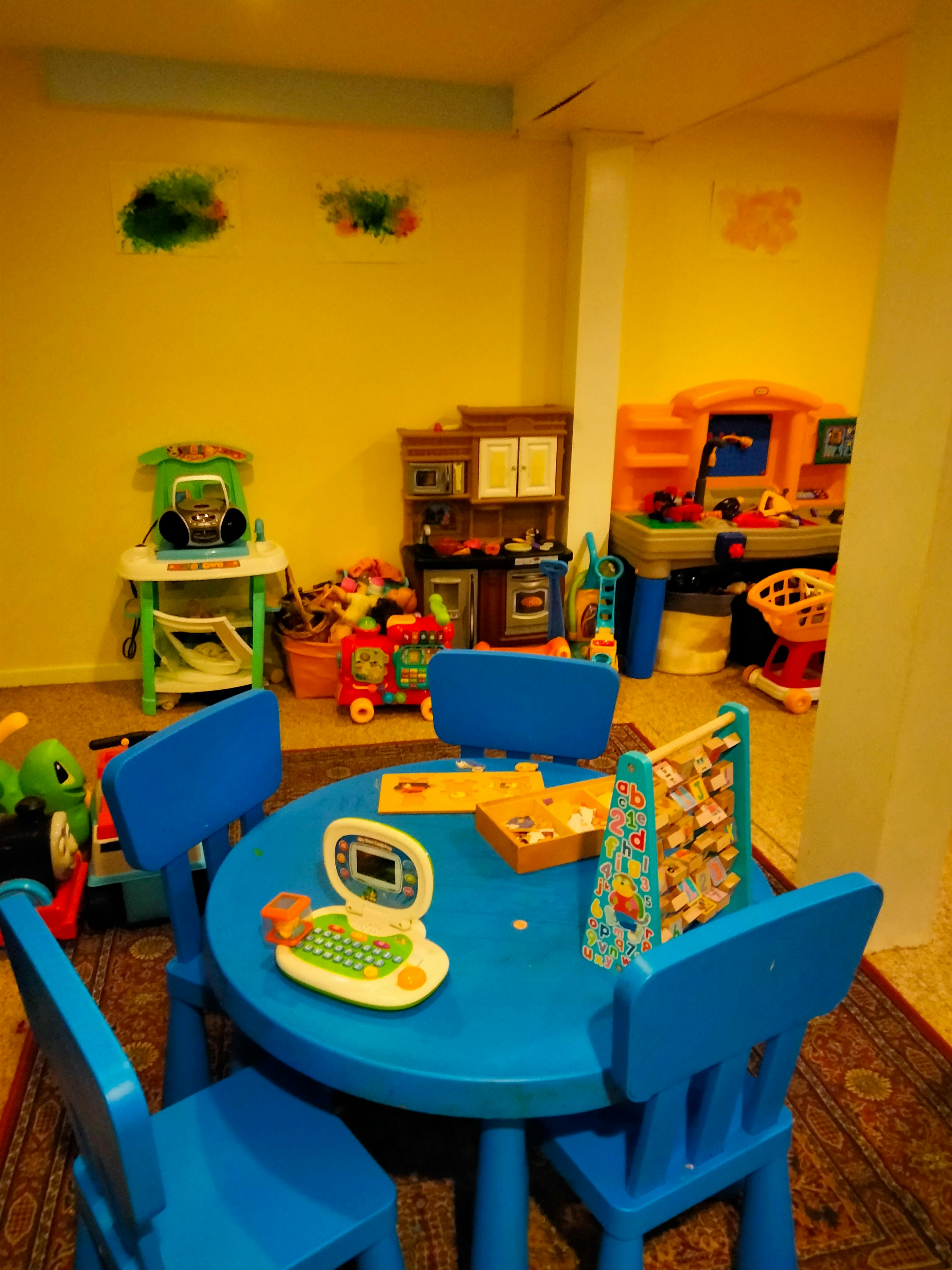 Playroom with a blue table and chairs, toys on the floor and shelves