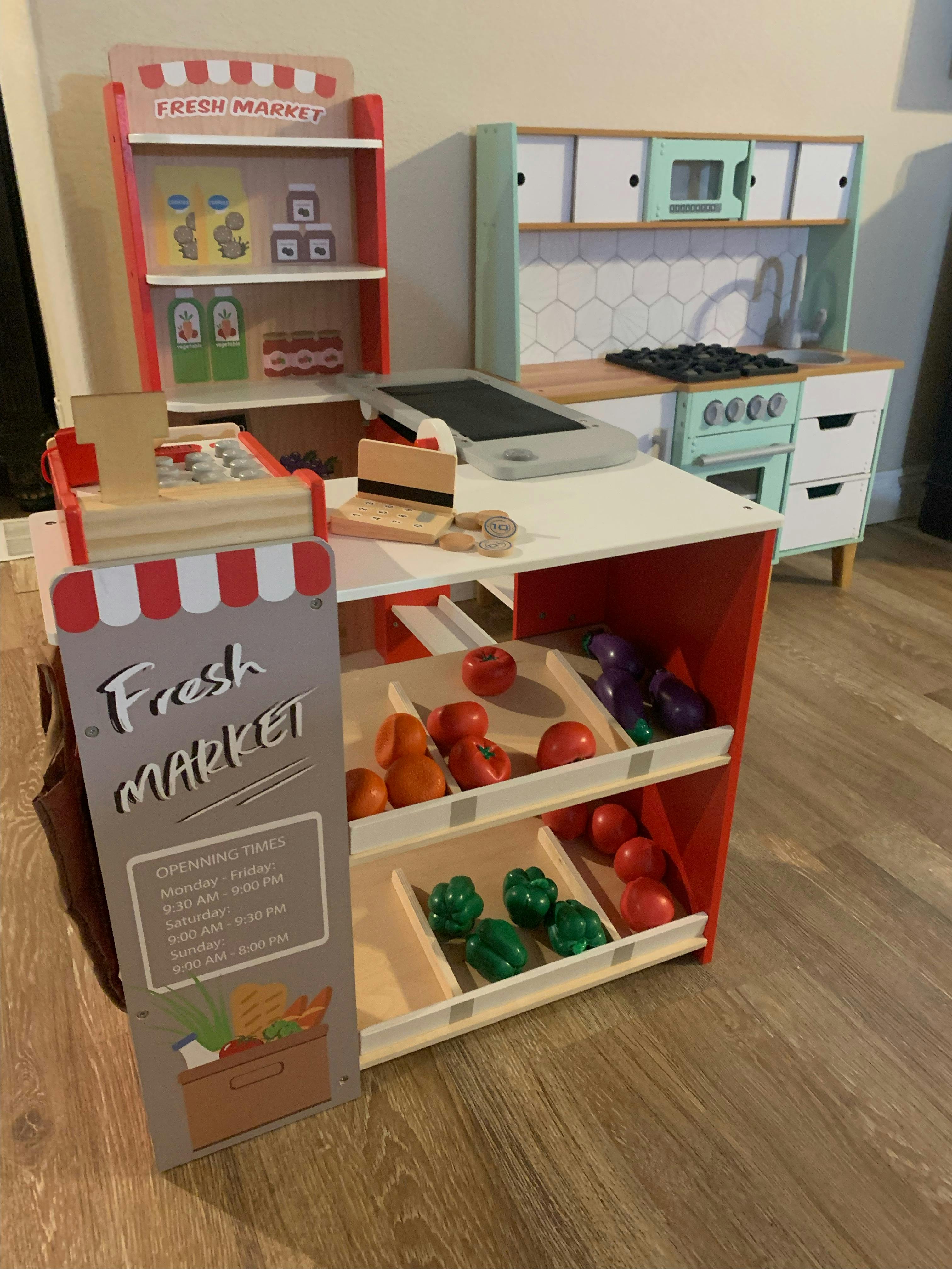 Toy fresh market stand with play food and a toy kitchen in the background