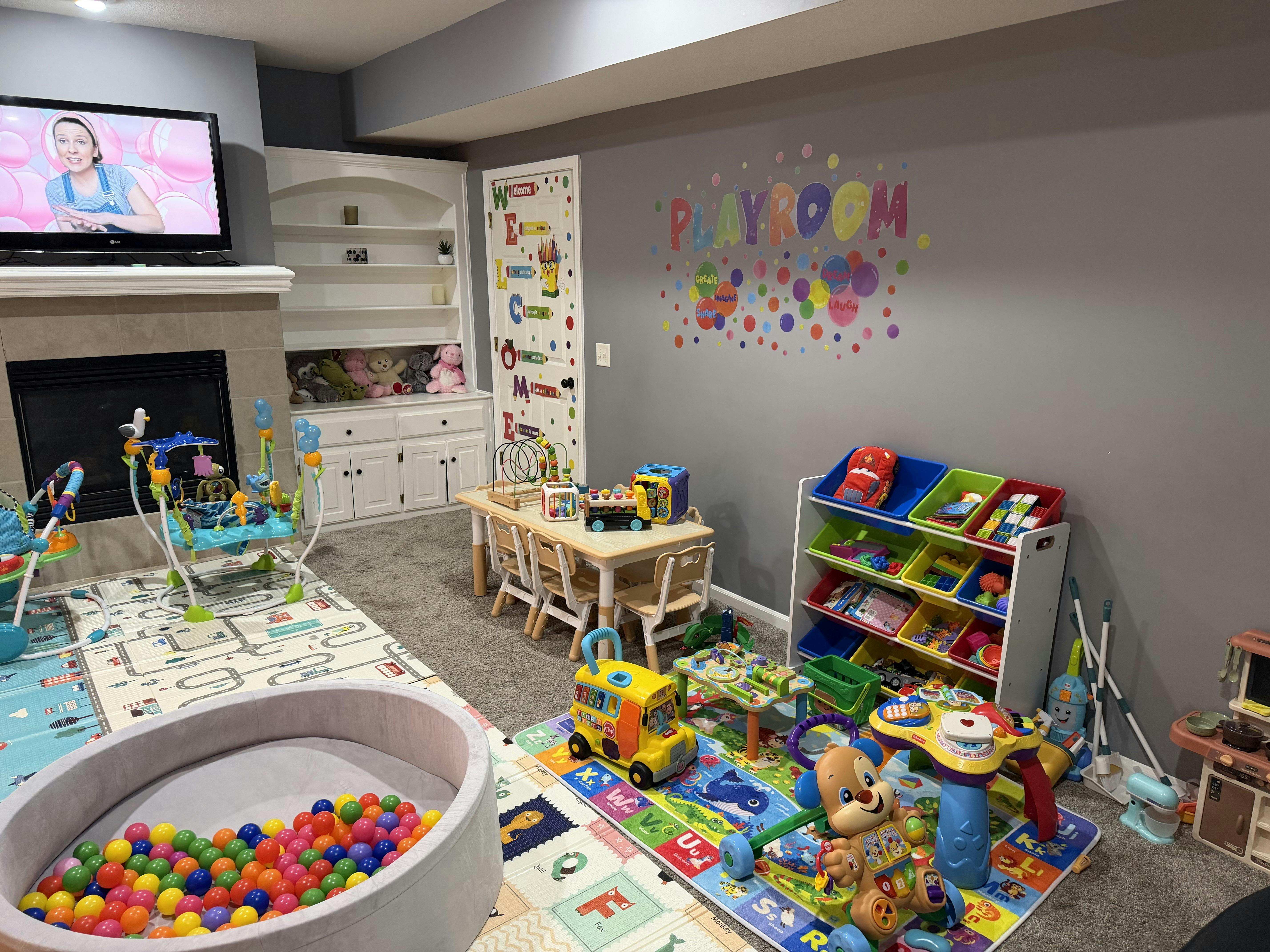 A playroom filled with toys, a ball pit, a play mat, and a TV showing a person