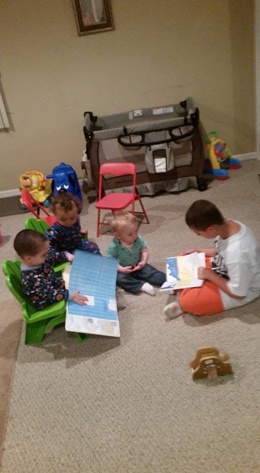 Four children sitting on a carpeted floor, reading books