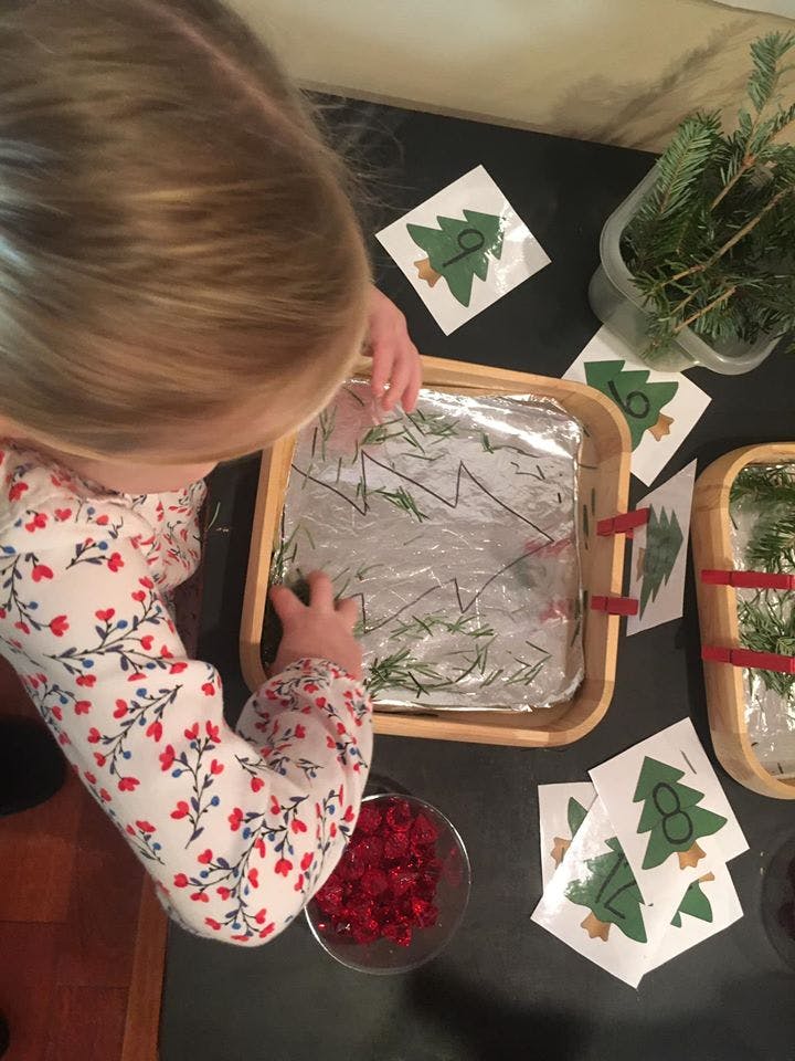 Child playing with pine needles and paper trees in a tray