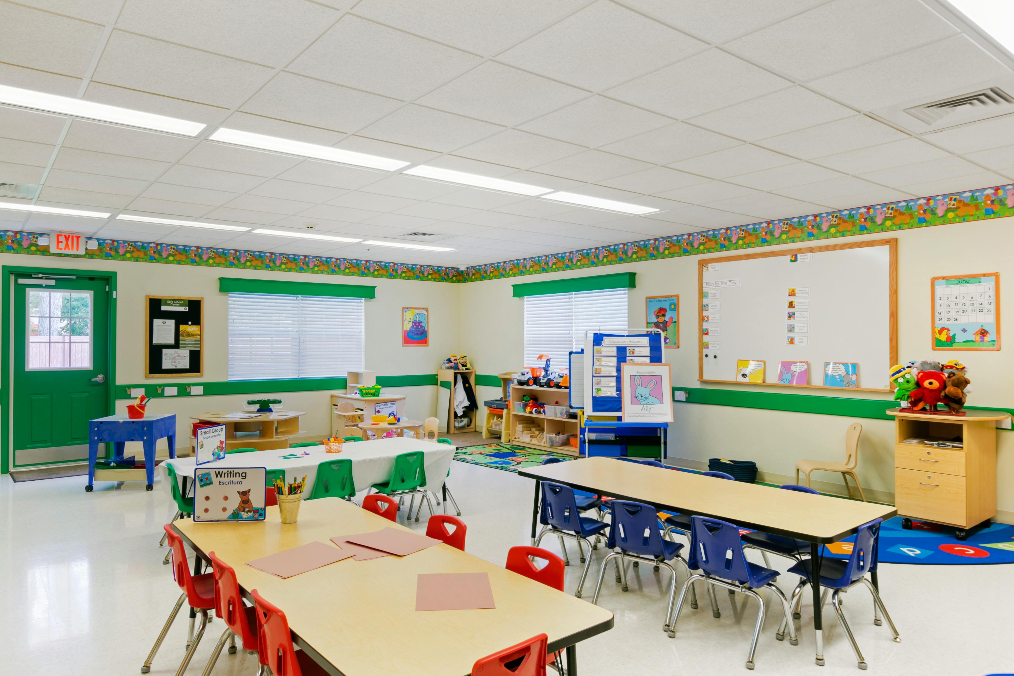 Empty classroom with small tables and chairs, whiteboard, and various learning materials
