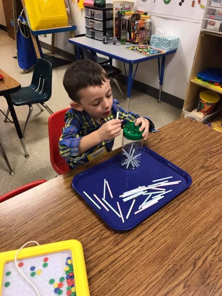Child playing with white sticks and a green container on a blue tray