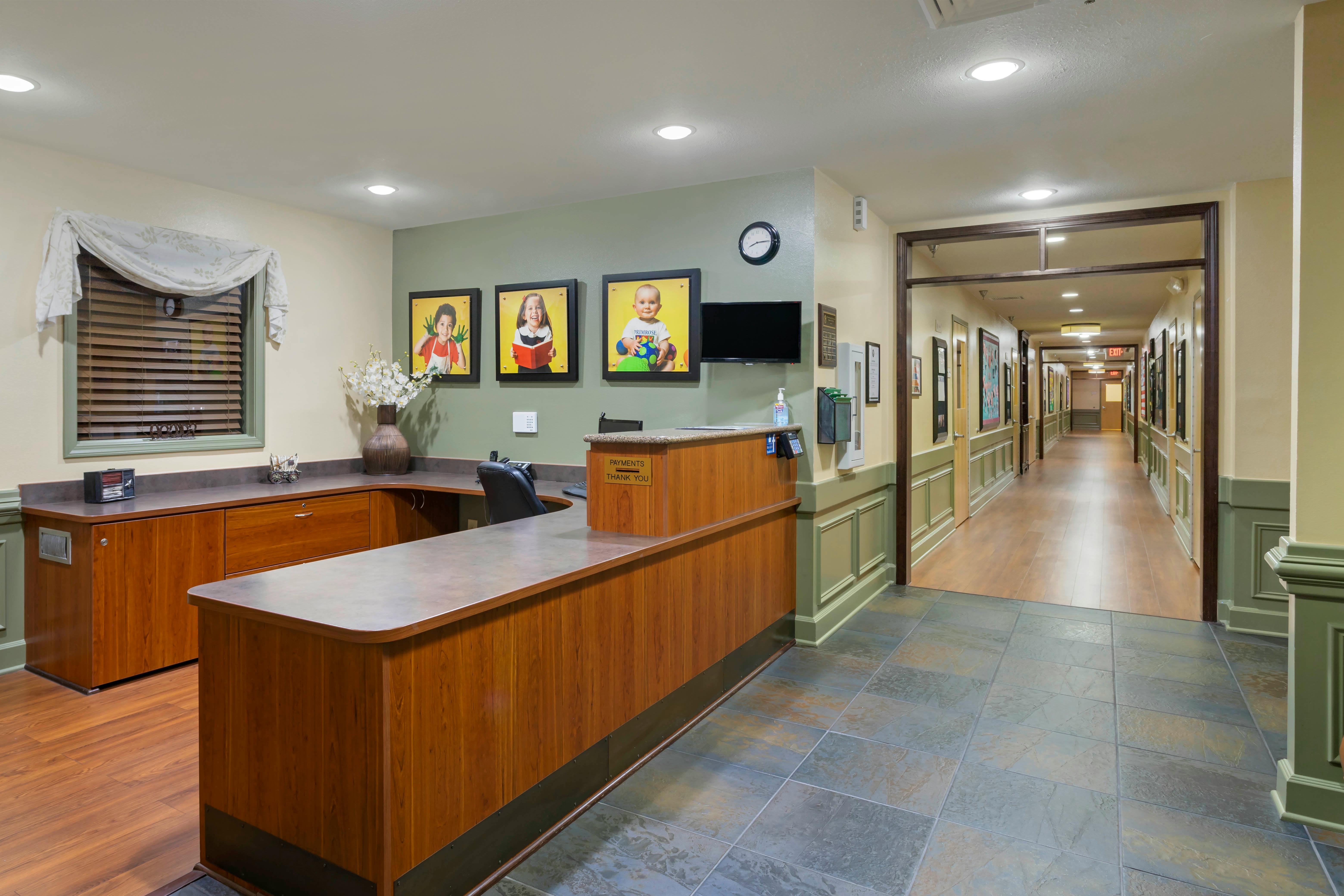 Reception desk with framed photos of children above it, and a hallway beyond