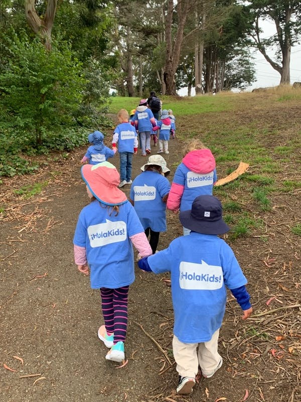 Group of children walking on a dirt path with “¡HolaKids!” on their shirts