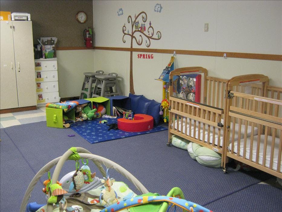 A colorful childcare room with cribs, play mats, and storage units