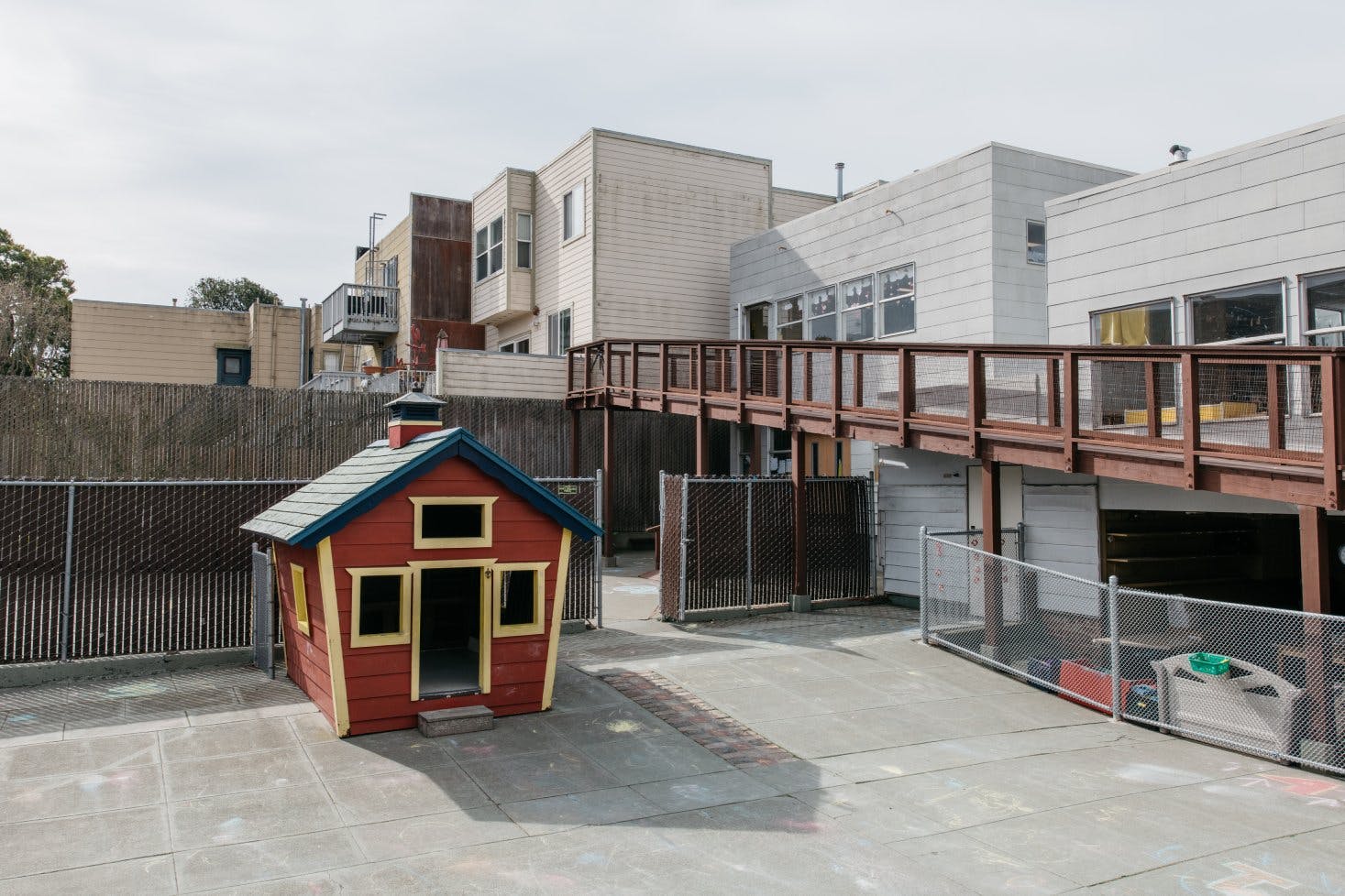 Red playhouse on concrete next to a chain link fence