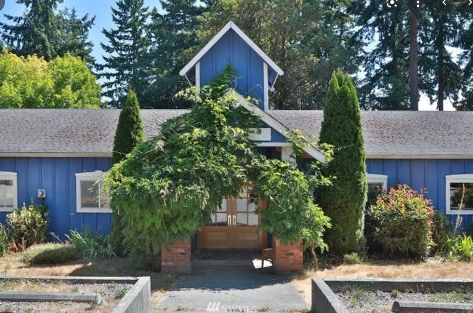 Blue building with a small gable and overgrown greenery around the entrance