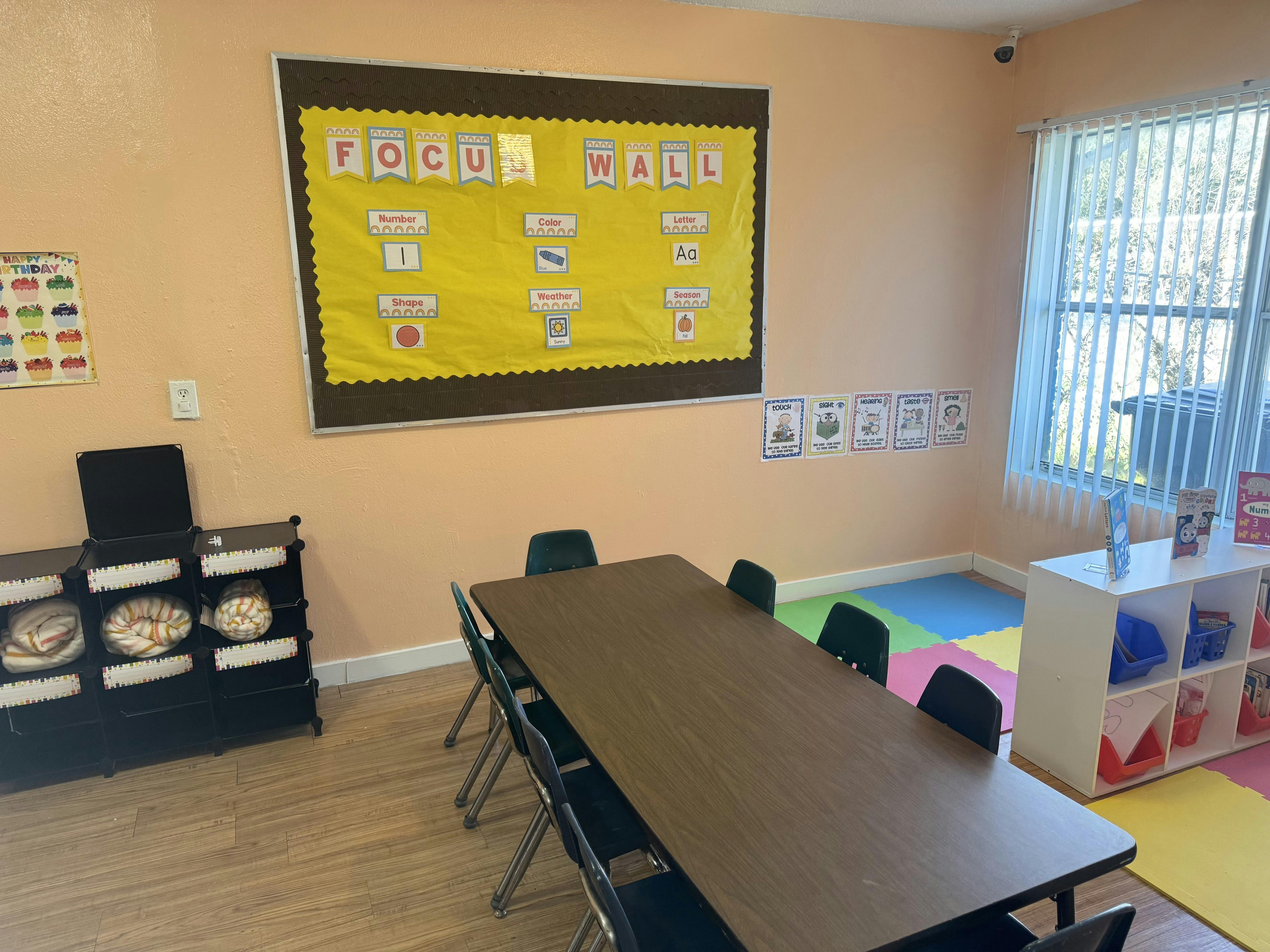 A classroom with a focus wall, a long table with chairs, and soft play mats