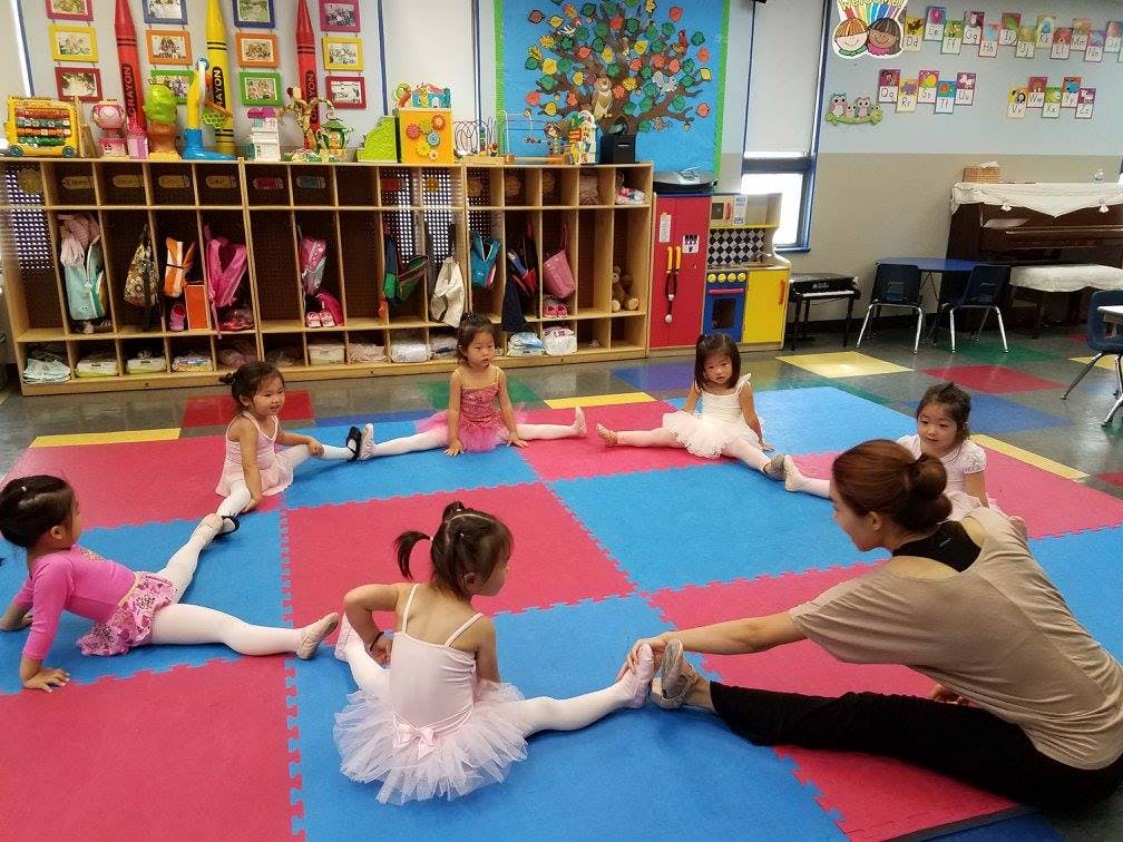 Adult and children in ballet attire stretching on a colorful mat