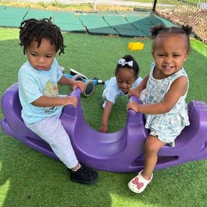 Three children playing on a purple seesaw