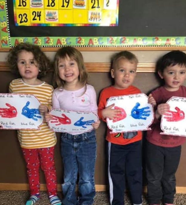 Four children holding up paper cutouts with handprints