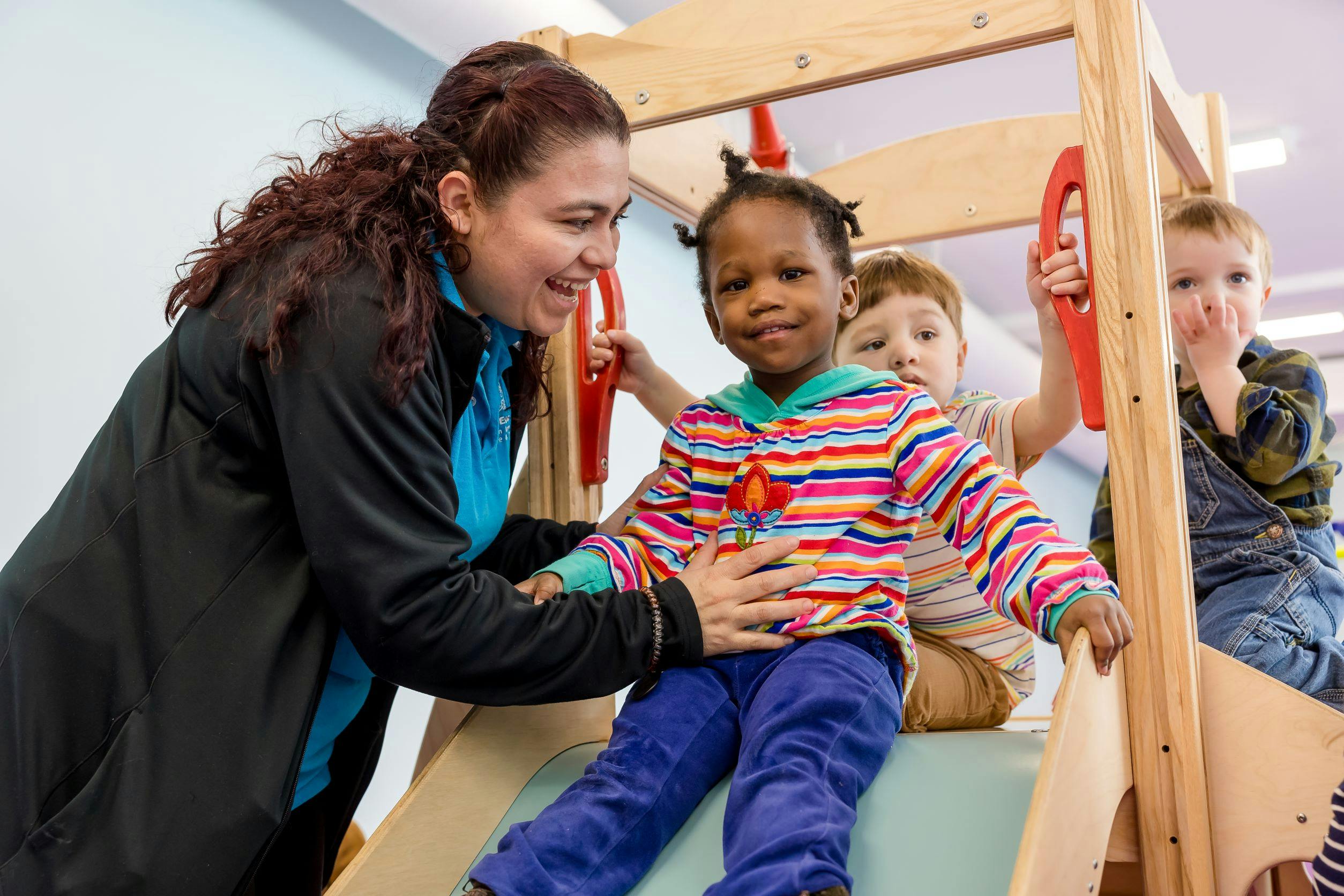 Adult helping a child on a slide with other children in the background