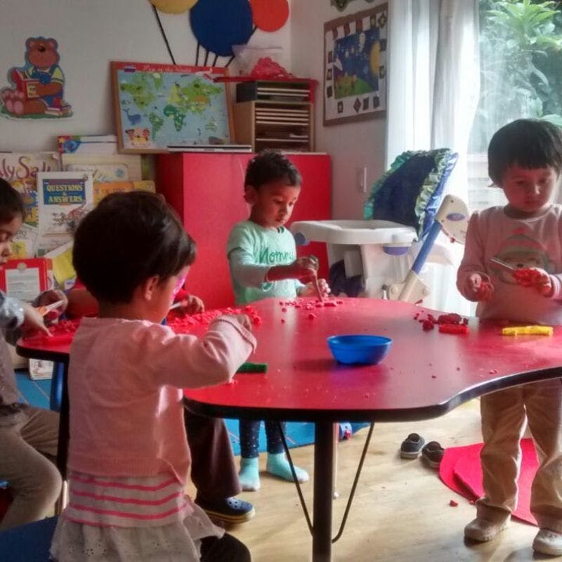 Children playing with small red blocks at a red table in a classroom