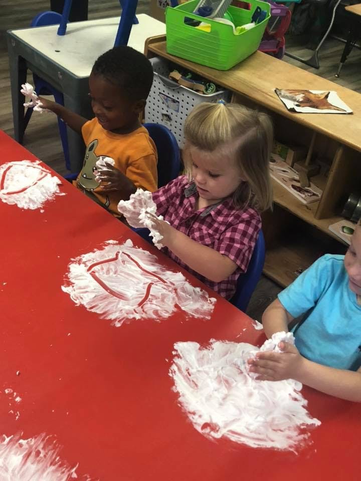 Three children playing with shaving cream on a red table