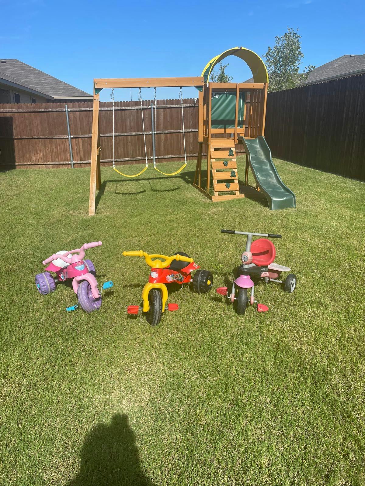 Playground set with swings and slide, with several tricycles on the grass
