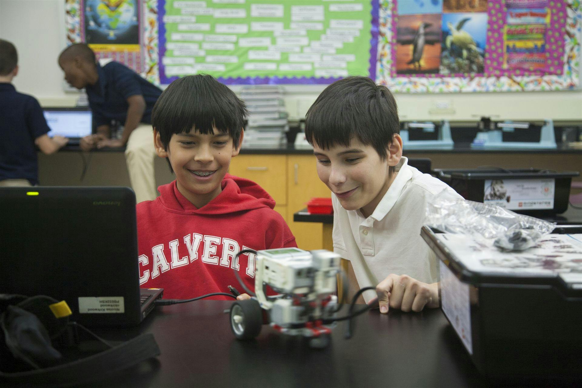 Two children working with a laptop and a small robot in a classroom