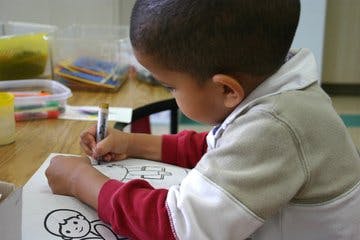 Child drawing on paper with a marker on a coloring page