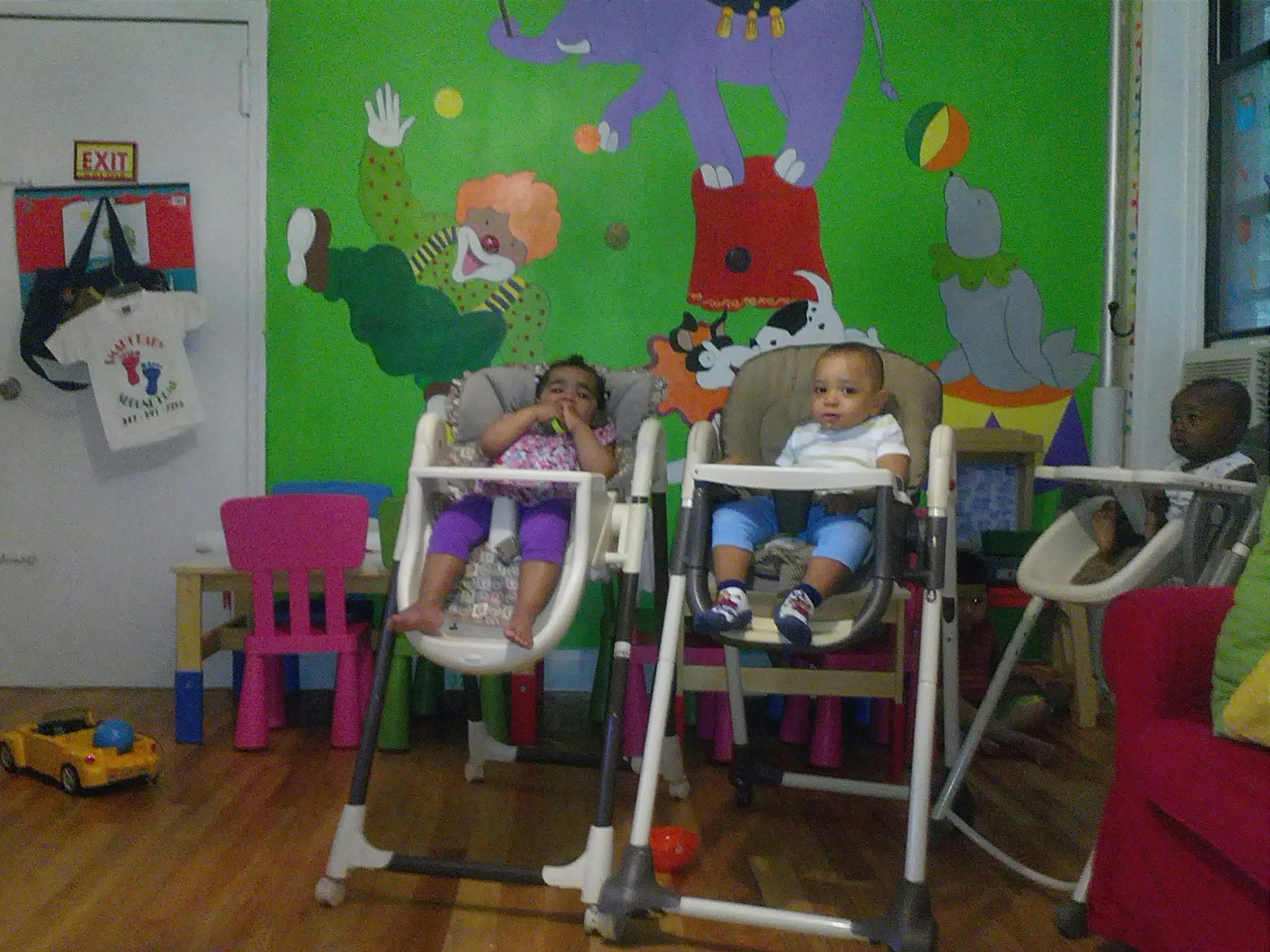 Three children sitting in high chairs in a room with colorful wall murals