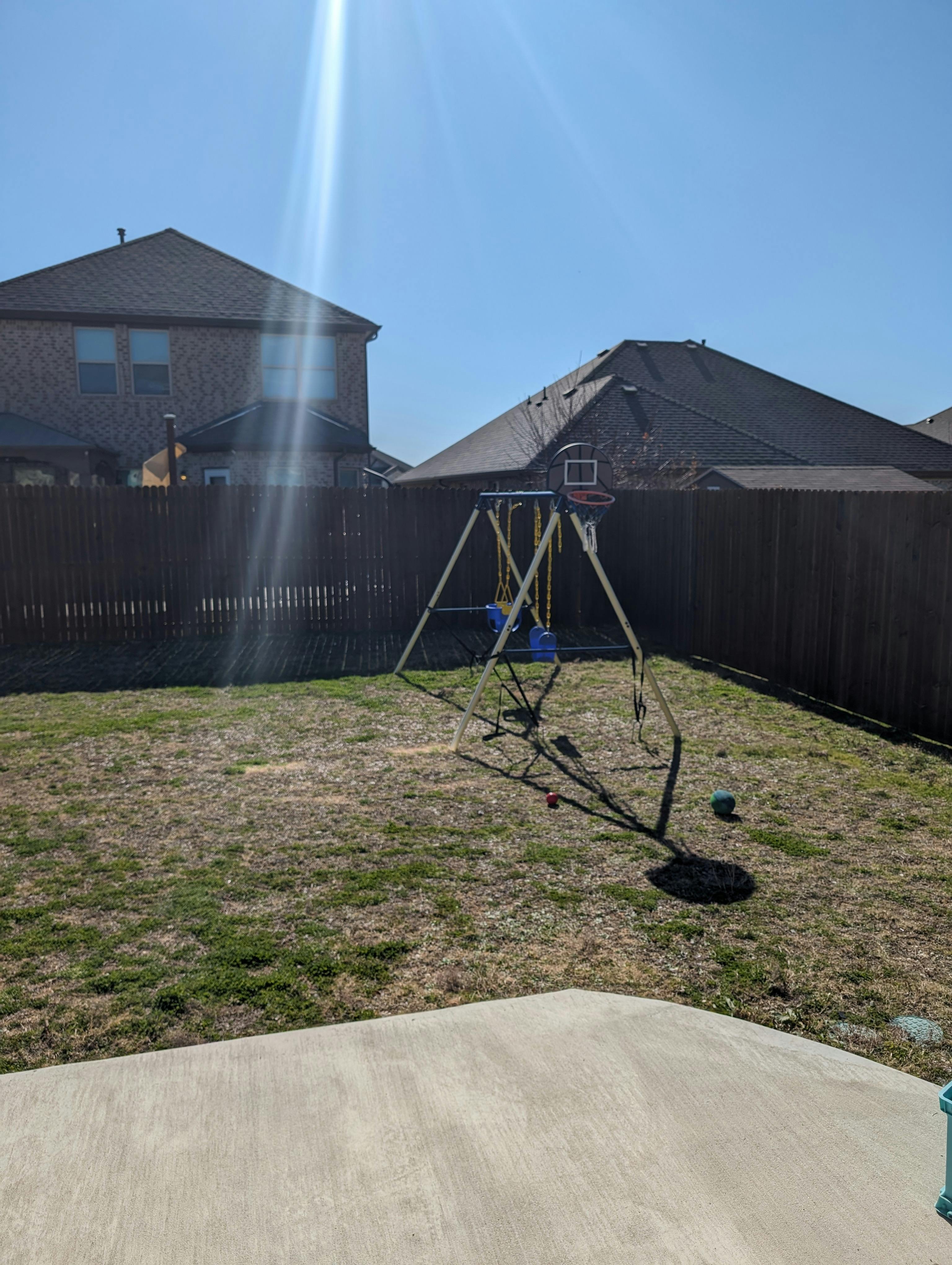Swing set in a backyard with houses and a fence in the background