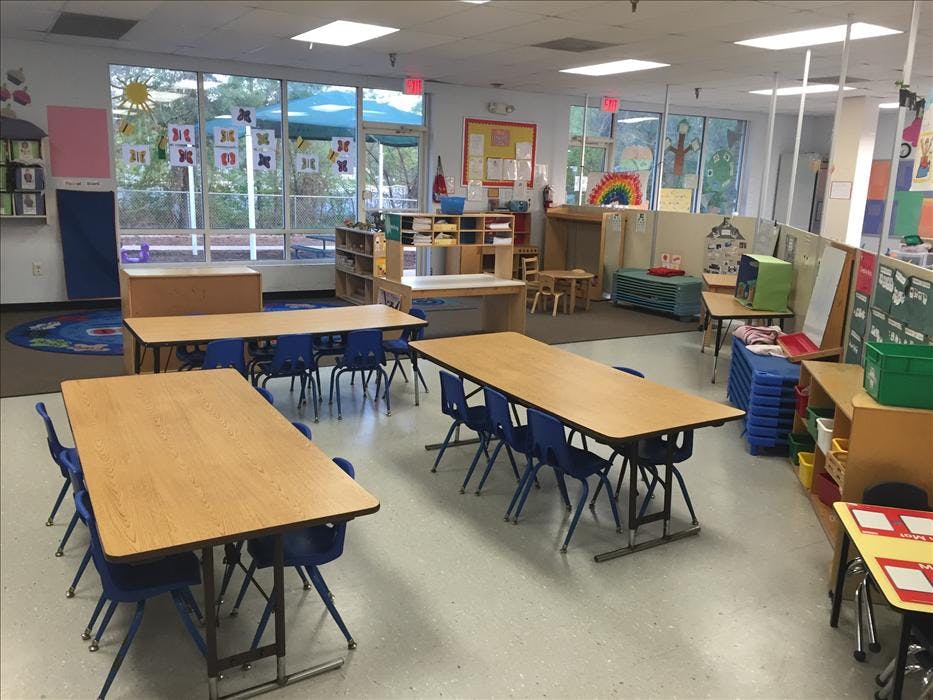 Classroom with multiple rectangular tables and blue chairs, and large windows