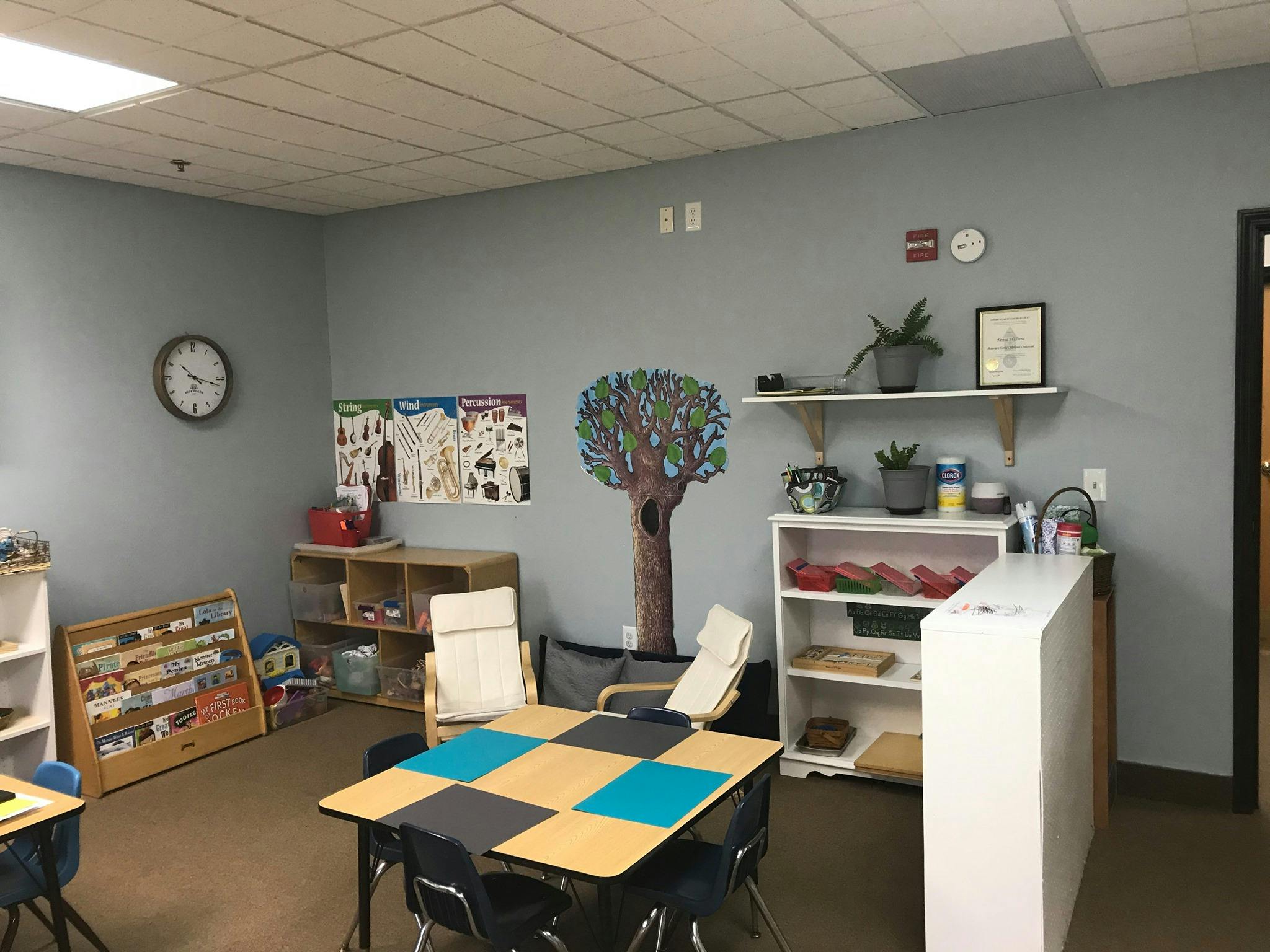 Classroom with tables, chairs, shelves, and a tree mural on the wall