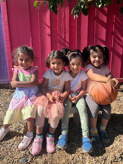 Four children sitting on a bench, one holding a basketball