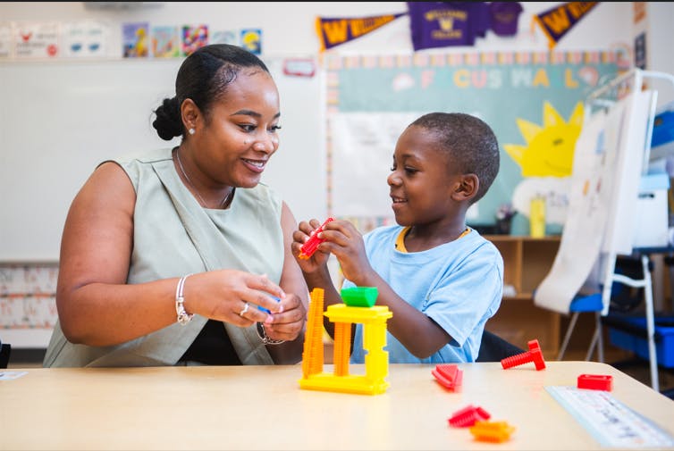 Adult and child playing with colorful building blocks in a classroom