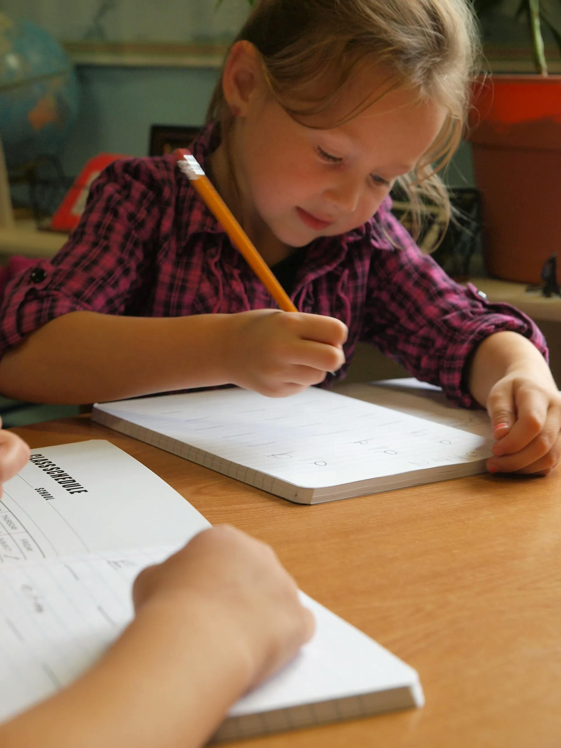 Child writing with a pencil on a notebook at a desk