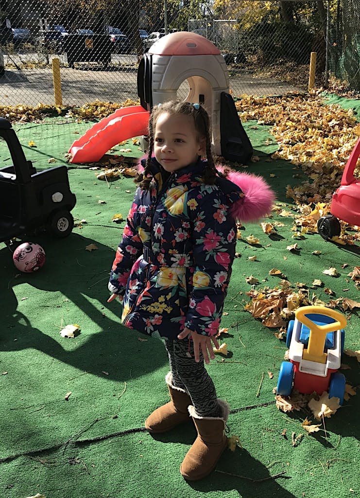 Child in a floral coat and boots standing on a playground