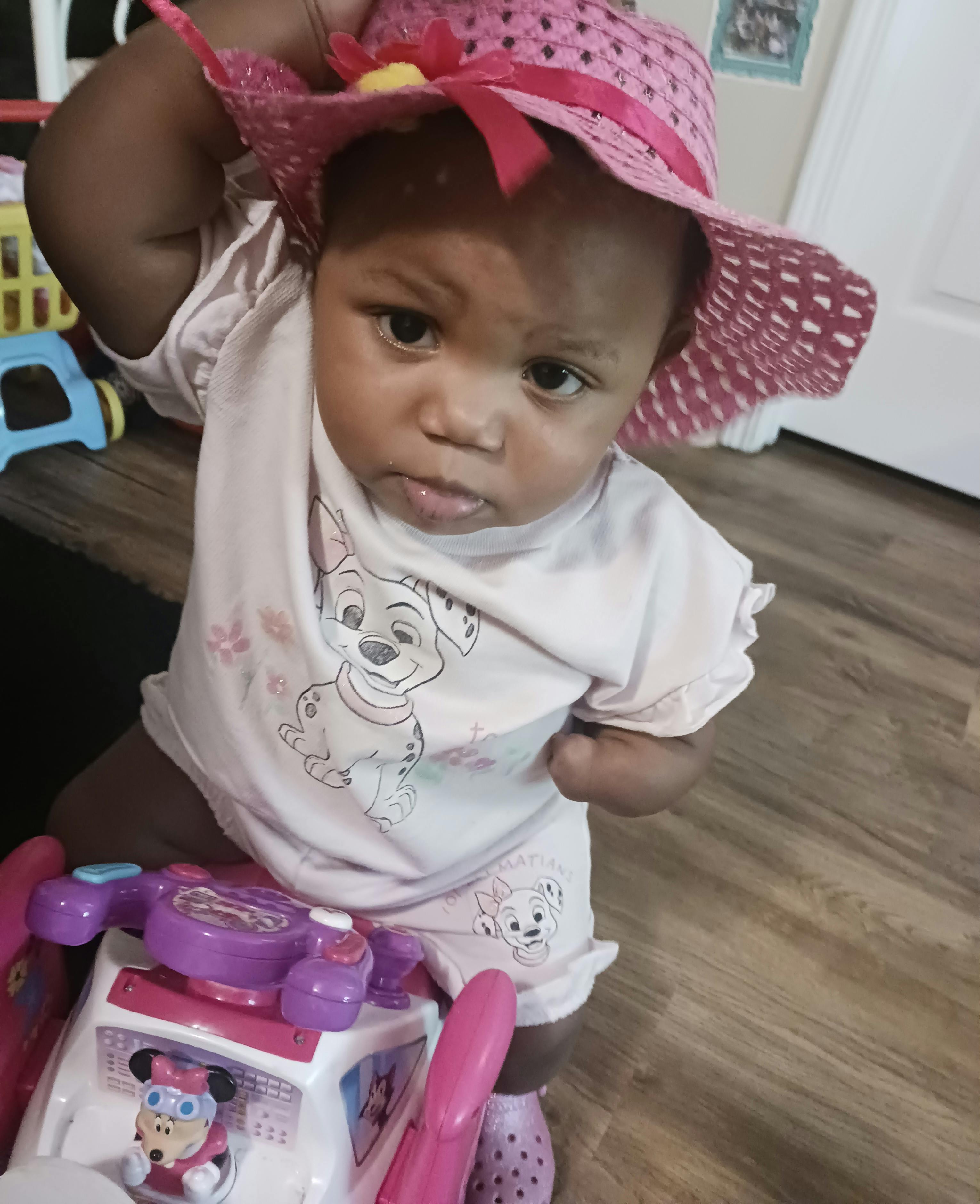 Child in a pink hat and shirt with Dalmatians on it, sitting on a toy