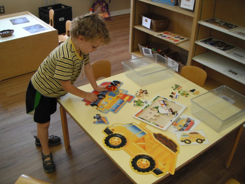 Child standing at a table assembling a puzzle