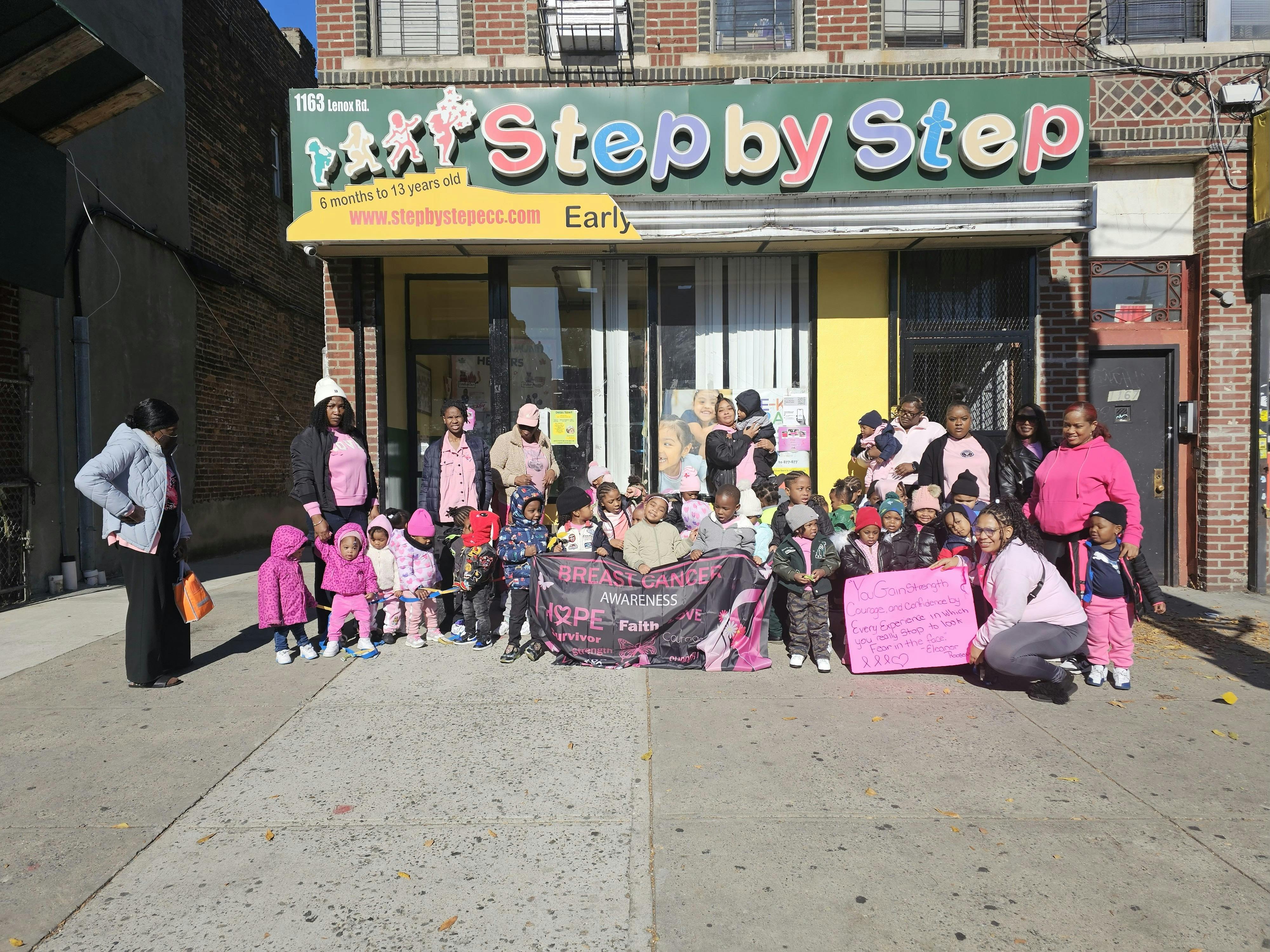 Group of people and children standing outside a building with a "Step by Step" sign
