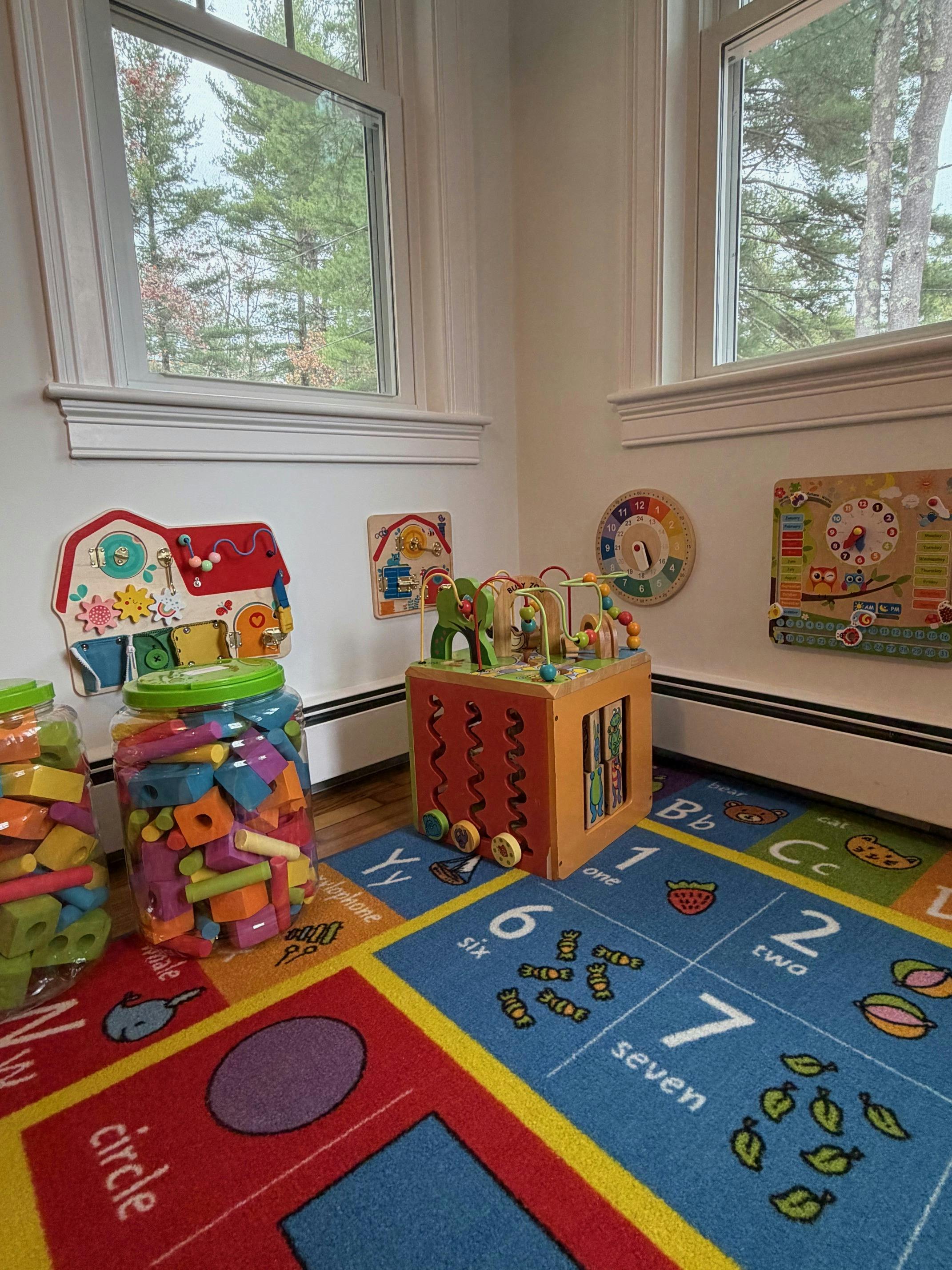 Playroom with a colorful rug, jars of blocks, and a wooden activity cube