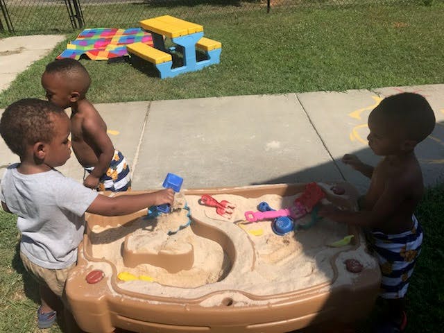Three children playing with a sand and water table outdoors