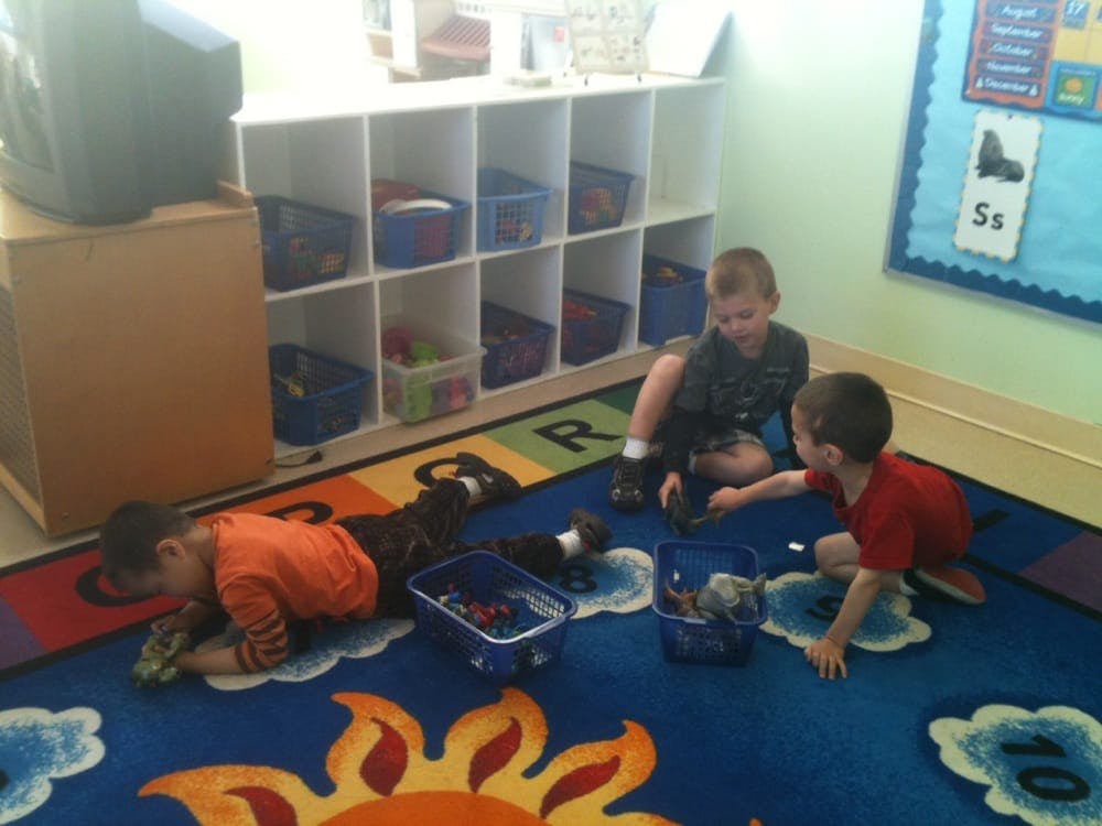 Three children playing on a colorful rug in a classroom