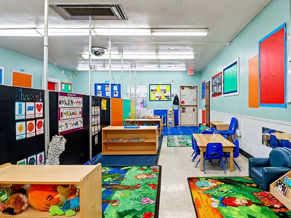 An empty classroom with colorful rugs, small tables, and educational charts on the walls