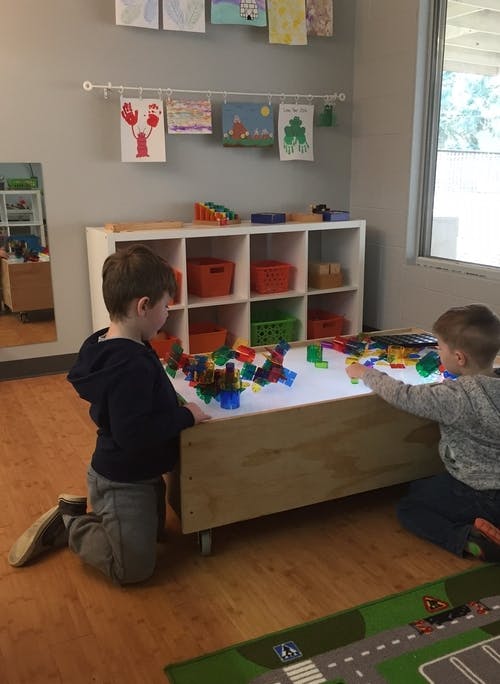 Two children playing with colorful blocks on a light table in a classroom