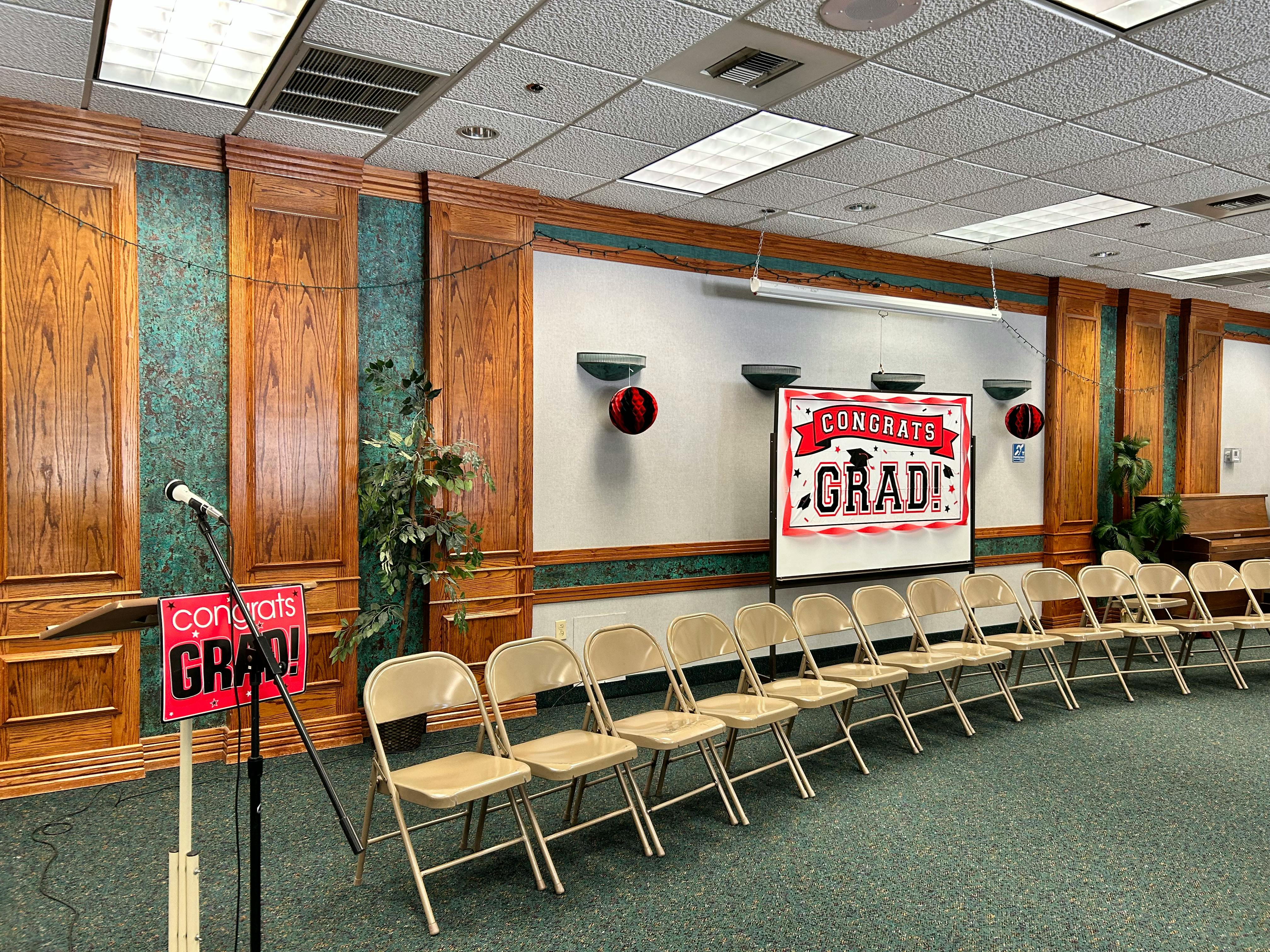 Empty chairs facing a screen with "Congrats Grad" sign in a room