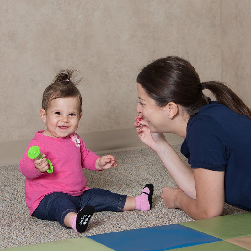 Adult and child on floor, child holding a green rattle