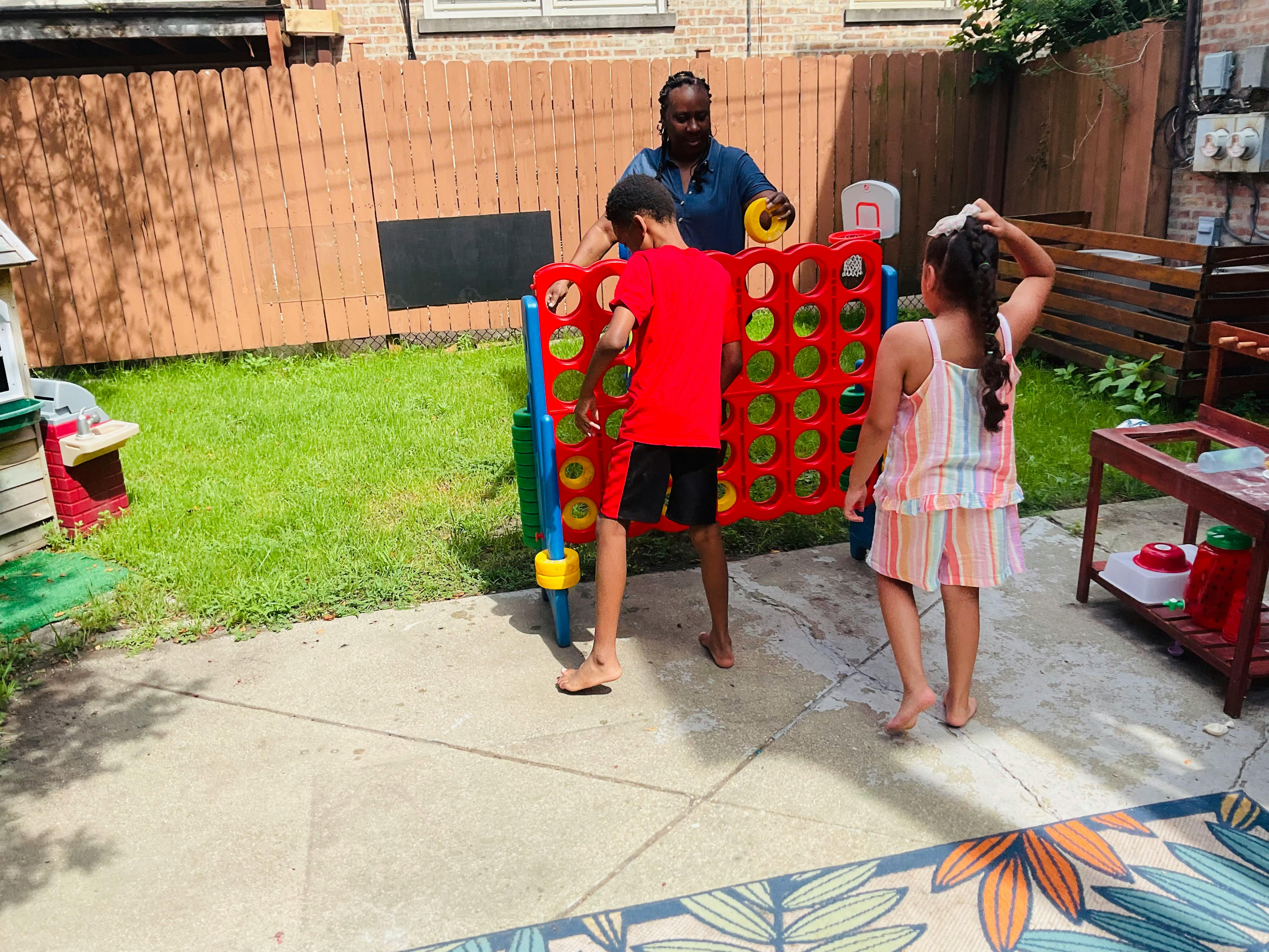 Adult and two children playing with a large standing ring toss game outdoors