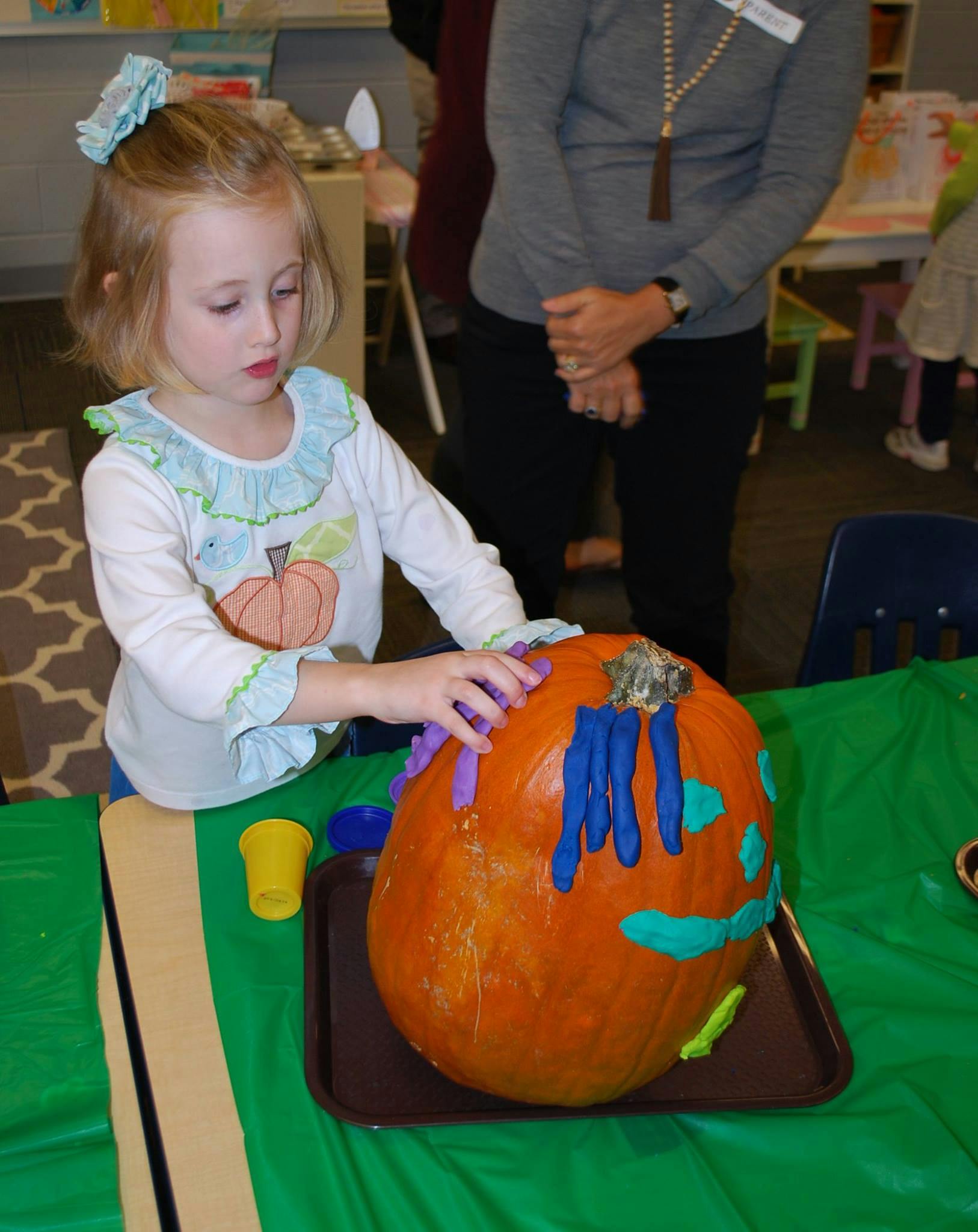 Child decorating a pumpkin with colorful clay