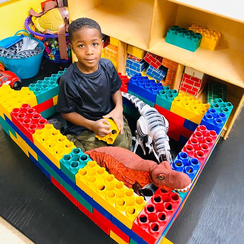 Child sitting in a play area made of large building blocks with toy dinosaurs