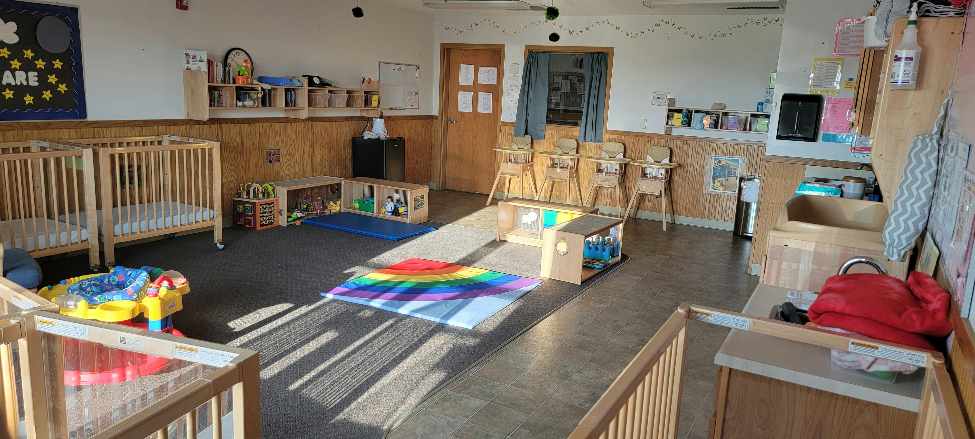 Empty classroom with cribs, play mats, and small furniture