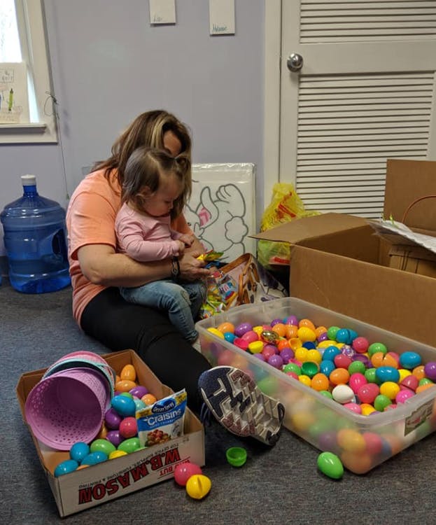 Person holding a child next to boxes of colorful plastic eggs