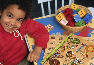 Child smiling next to a basket of alphabet blocks and a puzzle