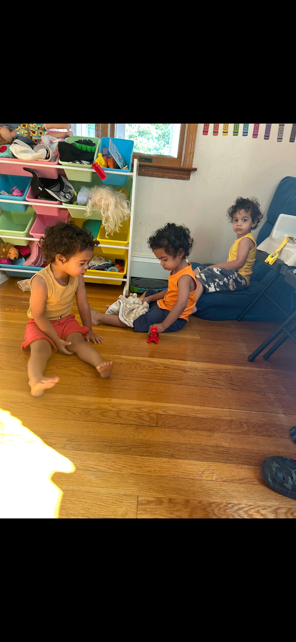 Three children sitting and playing on a wooden floor