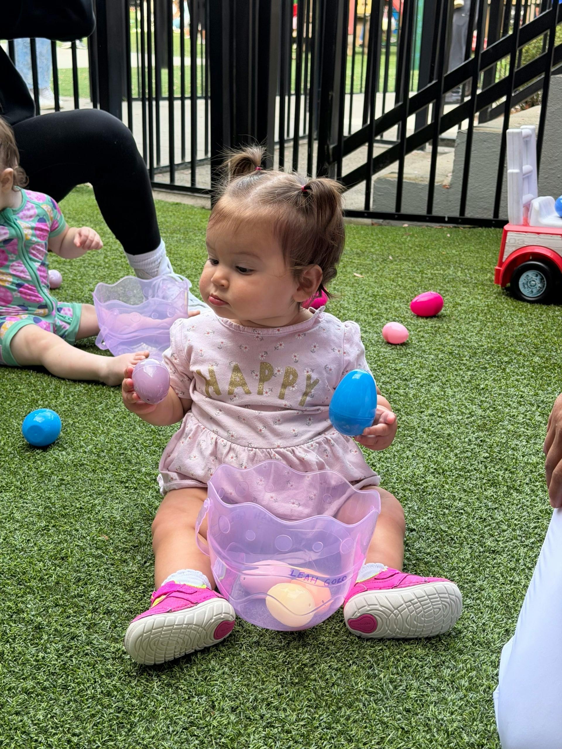 Child sitting on grass holding plastic eggs with a basket
